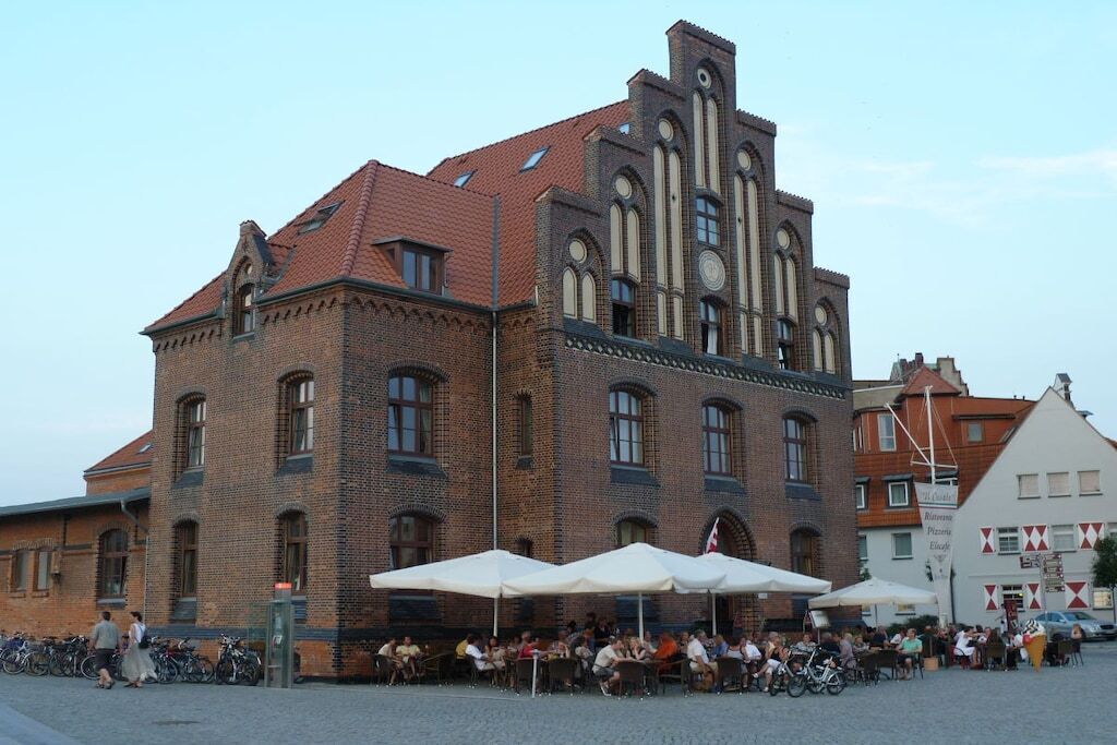 Een historisch gebouw met een bakstenen gevel en gebogen ramen, omringd door terrasjes en fietsen.