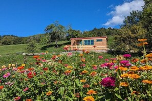 En træhytte med en træterrasse, omgivet af en have med forskellige blomster.