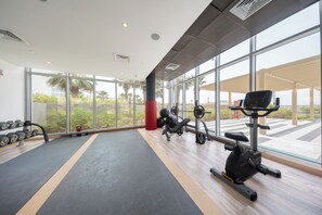 A gym with exercise equipment, large windows, and a view of the outdoors. - StayShort - Tranquil 1BR Hideaway in Damac Hills! (Damac Hills A)