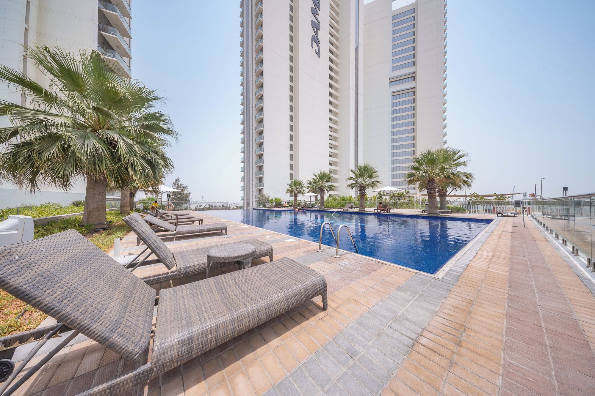 A rooftop pool area with lounge chairs, palm trees, and high-rise buildings in the background.