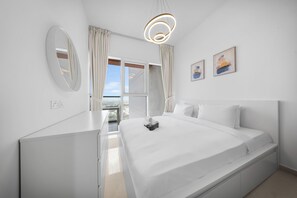 A modern hotel room with a large bed, a mirror, a view of the city, and a ceiling light fixture. - StayShort - Tranquil 1BR Hideaway in Damac Hills! (Damac Hills A)