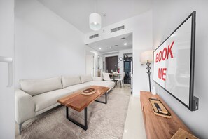 A modern living room with a sofa, a coffee table, and a TV mounted on the wall. - StayShort - Tranquil 1BR Hideaway in Damac Hills! (Damac Hills A)
