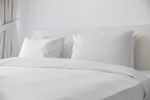 A neatly made bed with white bedding and pillows, a plain headboard, and a white wall. - StayShort - Tranquil 1BR Hideaway in Damac Hills! (Damac Hills A)