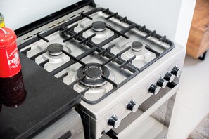 Cuina amb fogó a gas, ampolla vermella i aparell blanc.