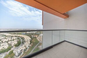 A high-rise building with a glass balcony overlooking a residential area with a curved road and greenery. - StayShort - Tranquil 1BR Hideaway in Damac Hills! (Damac Hills A)