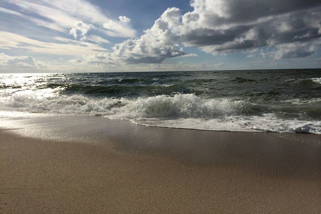 Una playa con olas acercándose a la orilla bajo un cielo parcialmente nublado.