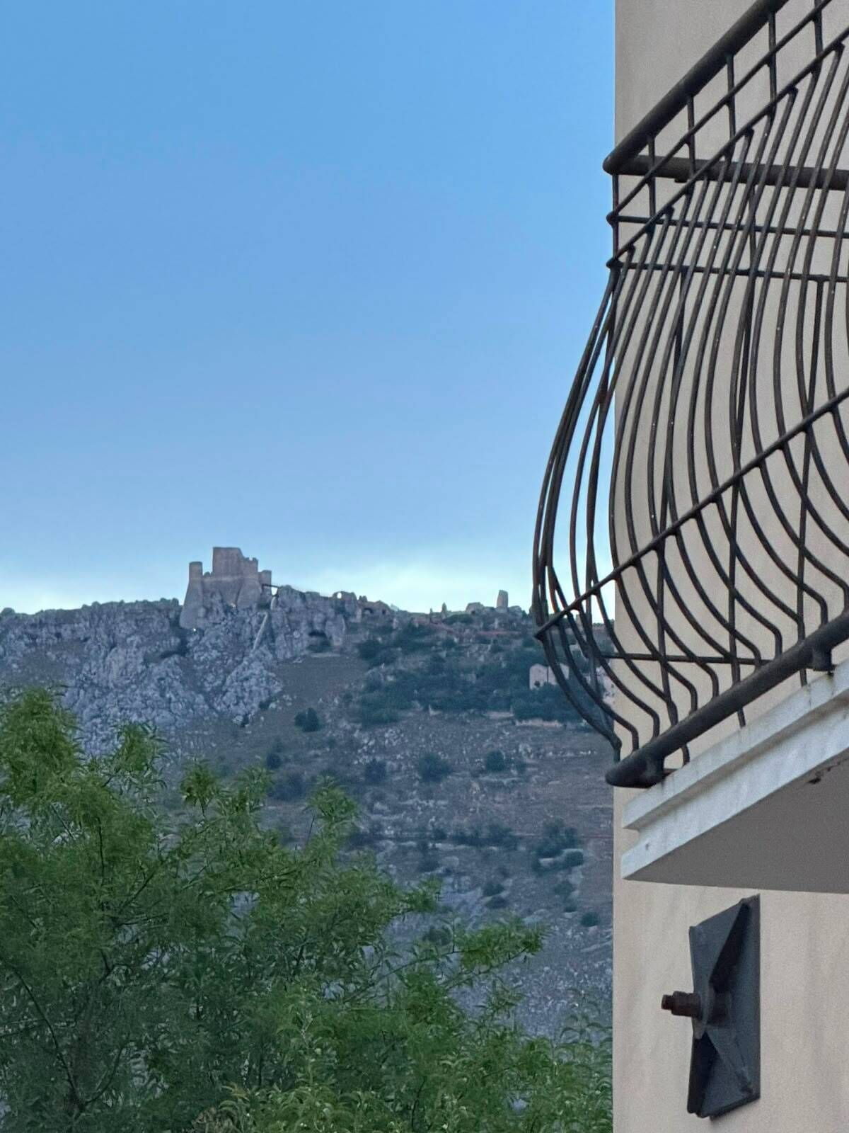 A building with a metal balcony overlooking a rocky landscape with ruins in the distance.