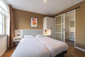 Ein modernes Schlafzimmer mit einem großen Bett, Nachttischen, einem Kleiderschrank und einer Glastür zum Badezimmer.