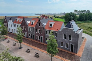 Eine Reihe von traditionellen und modernen Häusern mit roten Dächern, ein Sandstrand und Windkraftanlagen im Hintergrund.