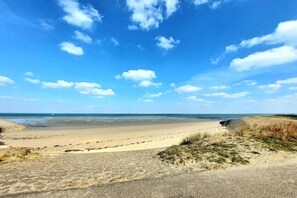 A beach with a clear sky, sandy shore, and a paved path leading to the water.