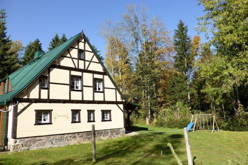 Un bâtiment traditionnel à colombages, doté d’un toit végétalisé, entouré d’arbres et d’une pelouse où se trouve une balançoire.