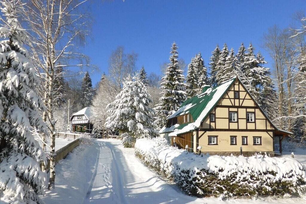 A traditional chalet with a sloped roof, surrounded by snow-covered trees and a clear sky.