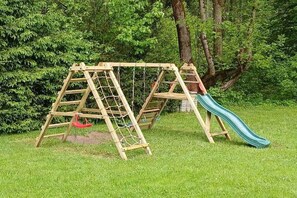 Un ensemble de jeux d’extérieur en bois, comprenant une balançoire et un toboggan, installé sur une pelouse, avec des arbres en arrière-plan.