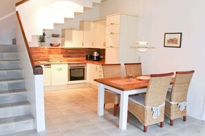 Una cocina moderna con armarios blancos, encimera de madera y un comedor con sillas de mimbre.