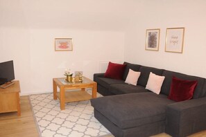 A living room with a grey sofa, a wooden coffee table, and a TV on a wooden stand. - Holiday apartment with 2 bedrooms (Lübeck)