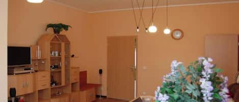 Una sala de estar con televisor, armarios de madera, una planta y una puerta.
