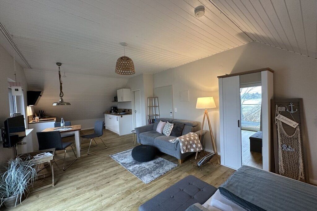 Un espacio habitable compacto con kitchenette, comedor, sofá, lámpara y un ventanal grande.
