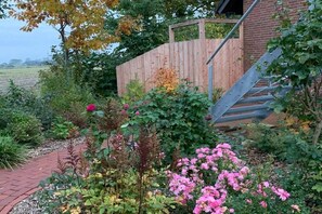 A garden with a brick pathway, flowering plants, and a wooden fence. - Apartment in Otterndorf with swimming pool (Otterndorf)