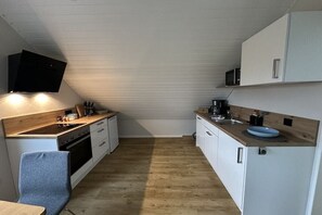 Eine kleine Küche mit einer Holz Arbeitsplatte, weißen Schränken, einer Mikrowelle und einem an der Wand befestigten Fernseher.
