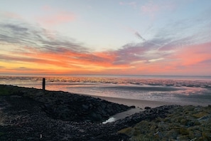 Eine Küstenlandschaft mit felsiger Uferlinie und einem sich im Abendrot spiegelnden Gewässer.