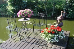 A deck with metal chairs and a table, surrounded by a pond with lily pads and a statue of a bird. - 2 Hein Garrn Fruit Farm (Mittelnkirchen)