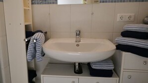 Casa de banho com lavatório branco, espelho e porta-toalhas.
