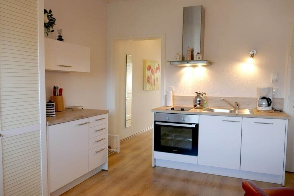 Eine kompakte Küche mit weißen Schränken, einem eingebauten Ofen und einer Arbeitsplatte mit einem Wasserkocher.