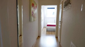 Corredor estreito com uma cama no final, um quadro na parede e uma janela com persianas.