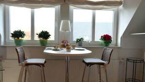 Uma sala de jantar com mesa redonda, duas cadeiras, abajur e plantas em vasos.