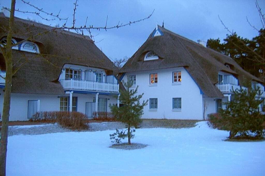 Une maison à deux étages, avec un toit de chaume, un balcon et un sol recouvert de neige.