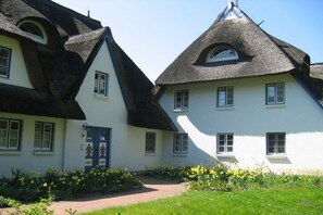 A traditional building with a thatched roof, a blue door, and a small garden with yellow flowers. - Achtern Diek “Sonneneck” (Zingst)