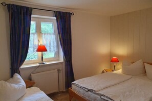 A bedroom with a bed, two bedside lamps, a window with curtains, and a radiator. - Achtern Diek “Sonneneck” (Zingst)
