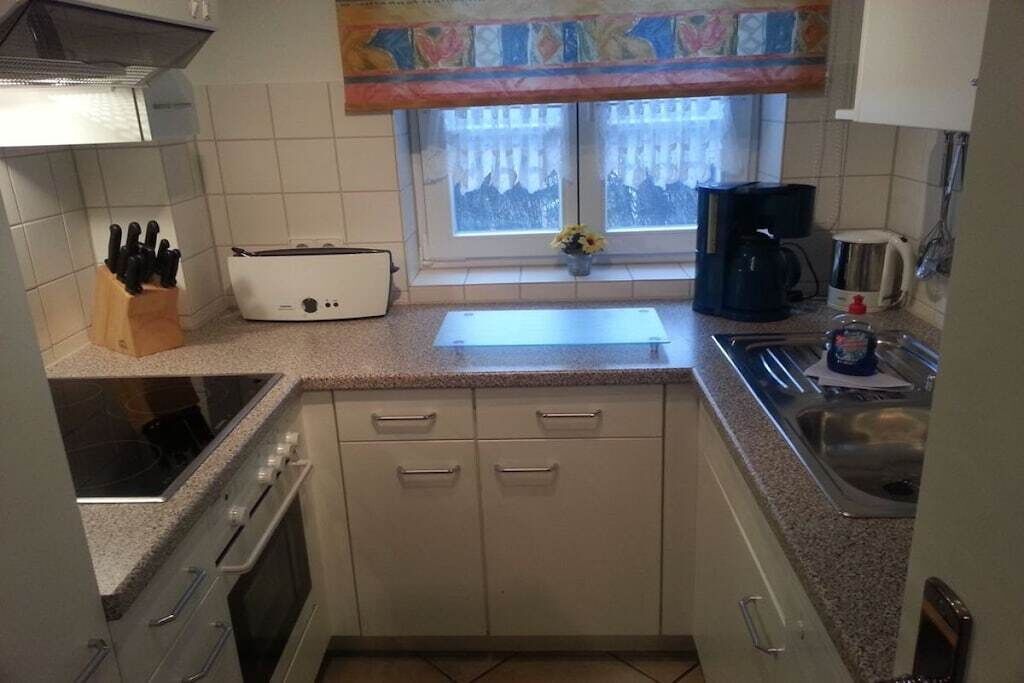 A compact kitchen with a stove, oven, sink, and a window with curtains.