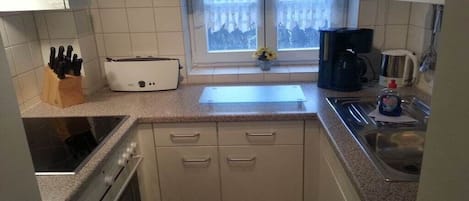 A compact kitchen with a stove, oven, sink, and a window with curtains.