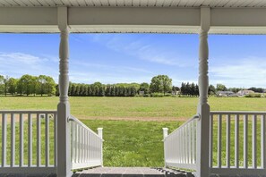 A covered porch with white railings and a view of a grassy field. - 6Br Spacious•HolidayFAMILYHOME (Williamsport)