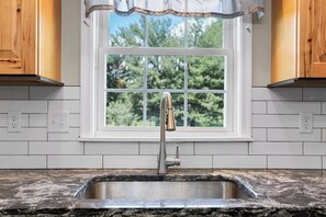 A kitchen with a stainless steel sink, white tiled backsplash, wooden cabinets, and a window with a view of trees. - 6Br Spacious•HolidayFAMILYHOME (Williamsport)