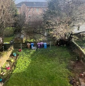 A grassy yard with a fence, a tree, and several trash bins.