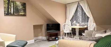 A compact living space with a sofa, a small table, a TV, and a window with curtains.