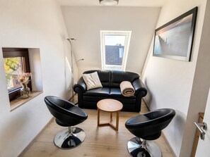 Ein modernes Wohnzimmer mit einem schwarzen Ledersofa, zwei schwarzen Sesseln, einem Holztisch, einer Stehlampe und einem gerahmten Bild an der Wand.