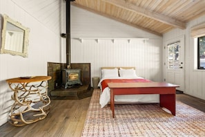 A room with a bed, a wooden table, a fireplace, and a door with a window. - Rancho de los Venados (Santa Ynez)