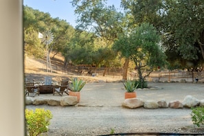 An outdoor seating area with chairs and planters, surrounded by trees and a fenced enclosure. - Rancho de los Venados (Santa Ynez)