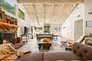 A spacious living area with a stone fireplace, a television, and a comfortable seating arrangement. - Rancho de los Venados (Santa Ynez)