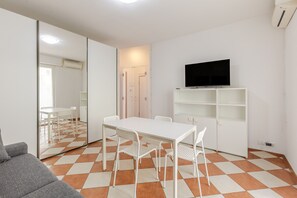 A modern living room with a white sofa, a dining table with chairs, a flat-screen TV mounted on a white shelf, and a large mirror reflecting the room. - Zip House Apartment Verona (Verona)