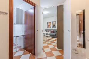 Un couloir avec un sol à carreaux, une porte en bois et une vue sur un salon comprenant un canapé et une table.