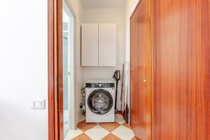 Une buanderie équipée d’un lave-linge, d’un étendoir et d’un meuble de rangement placé au-dessus du lave-linge.