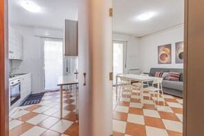 A modern kitchen with white cabinets, a dining area with a white table and chairs, and a living room with a sofa and abstract wall art. - Zip House Apartment Verona (Verona)