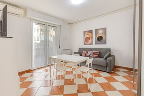 Un salon moderne avec un canapé gris, une table et des chaises blanches, un radiateur et des œuvres d’art accrochées au mur.