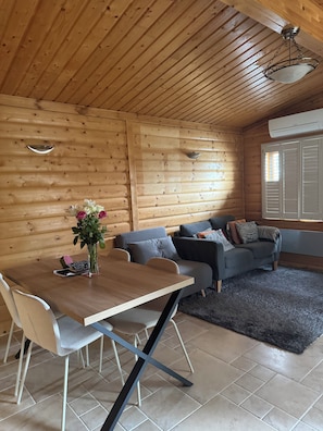 A wooden interior with a dining table, chairs, a sofa, and a decorative vase.