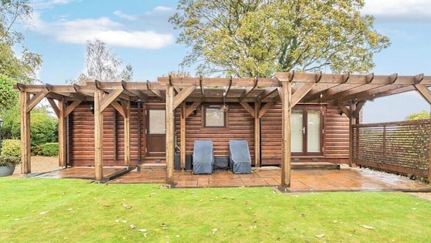 Eine Holz-Pergola mit einer Terrasse, zwei Stühlen und einem Holzzaun.