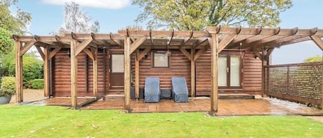 A wooden pergola structure with a patio area, two chairs, and a wooden fence.